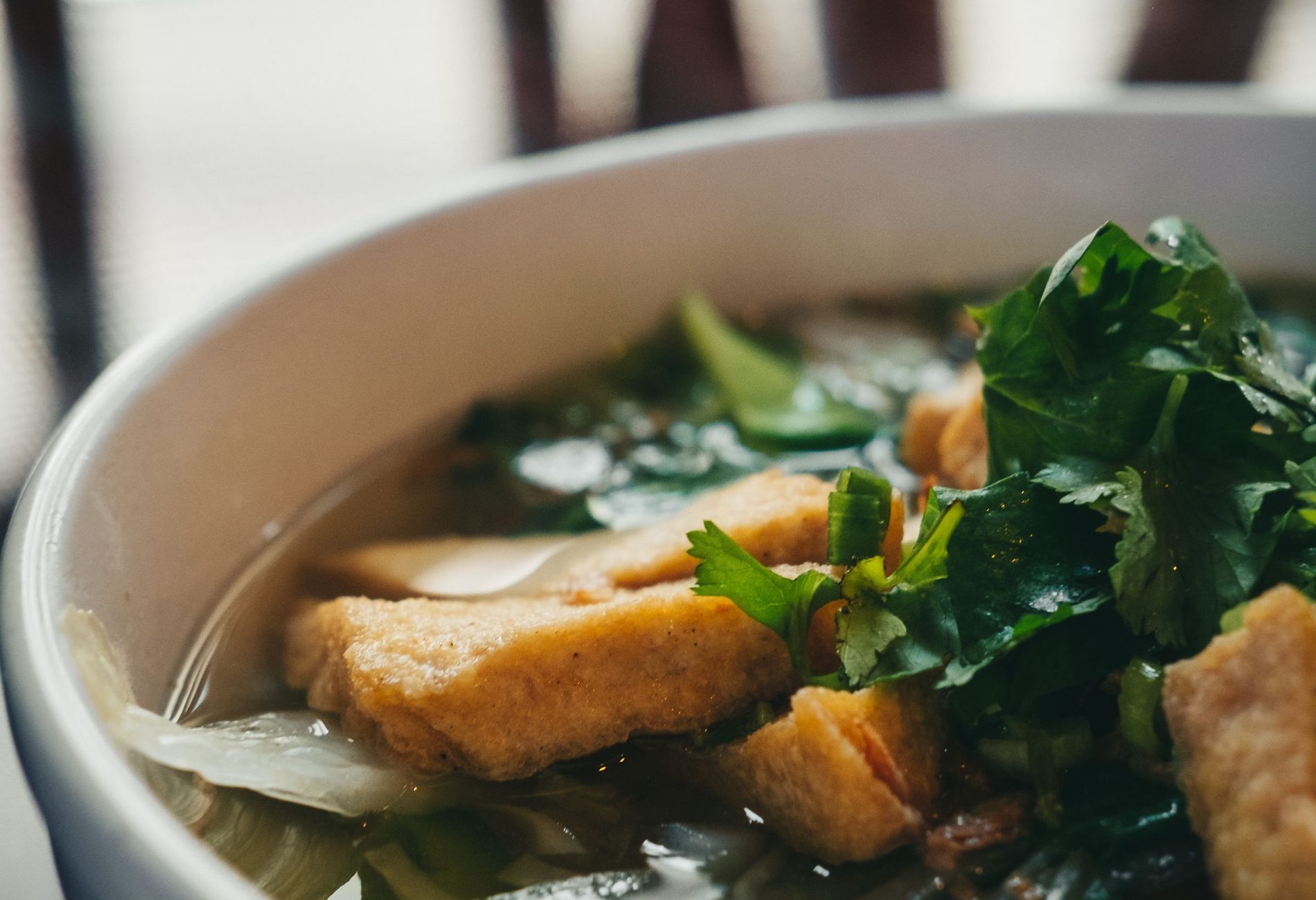 Bowl of Vietnamese pho with fresh herbs and coriander, steam rising